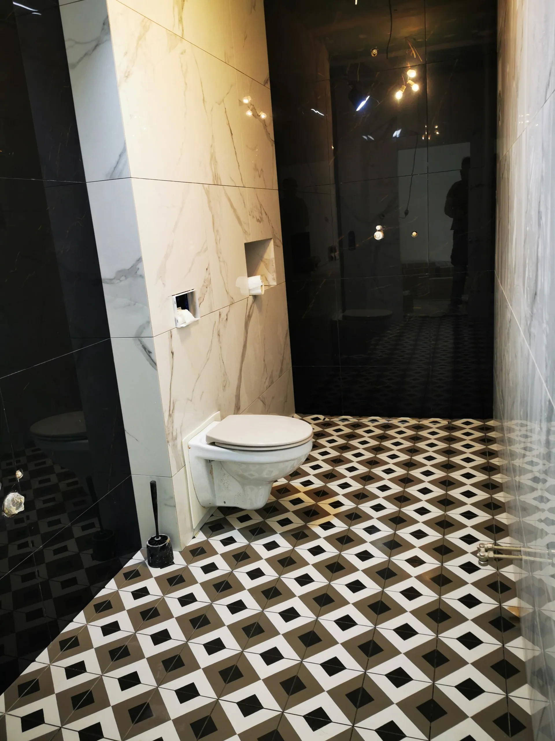 Szersze ujęcie gotowej łazienki z WC podwieszanym, wnęką podtynkową i mocno wzorzystą podłogą.